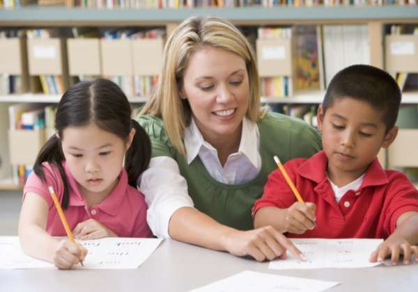 Young blonde teacher helping two kindergarten students
